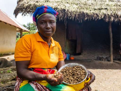 In Sierra Leone, outside her home and farm, Maryama smiles holding a bowl of her ground nut harvest.