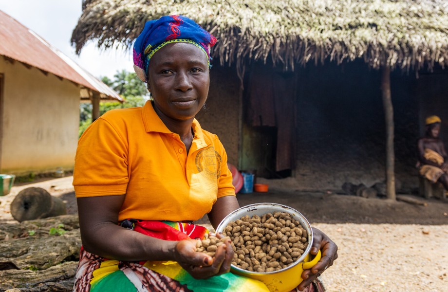 In Sierra Leone, outside her home and farm, Maryama smiles holding a bowl of her ground nut harvest.